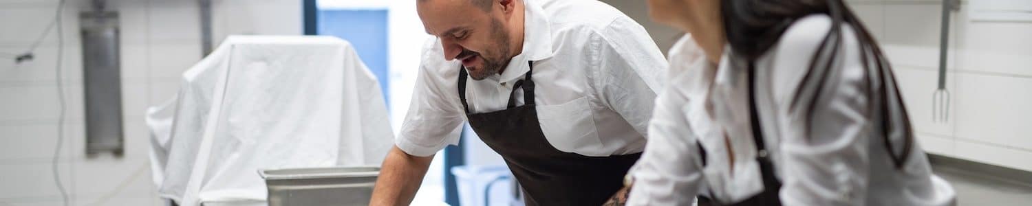 A chef and cook cleaning the workspace after doing dishes indoors in restaurant kitchen.
